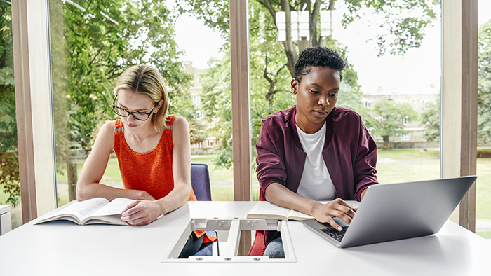 one female and one male students studying together, one using a book the other a laptop.